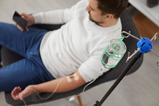 Man reclining in a chair using his smartphone while receiving IV hydration therapy in Gilbert