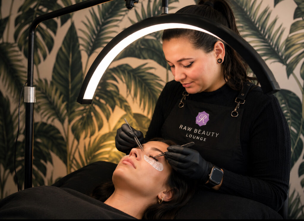 lash extensions salon Lash artist applying extensions with a palm leaf wall behind her